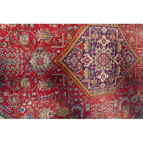 1075 - An antique Persian wool rug with medallion design on a red field with blue borders, 210 x 312cm