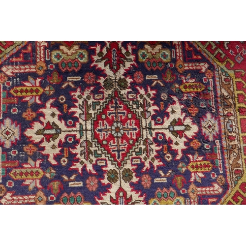 1075 - An antique Persian wool rug with medallion design on a red field with blue borders, 210 x 312cm