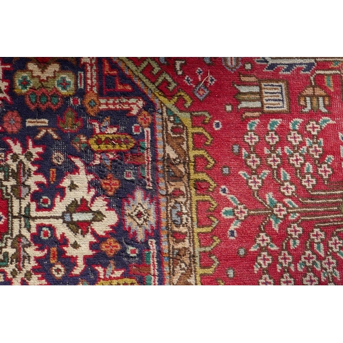 1075 - An antique Persian wool rug with medallion design on a red field with blue borders, 210 x 312cm