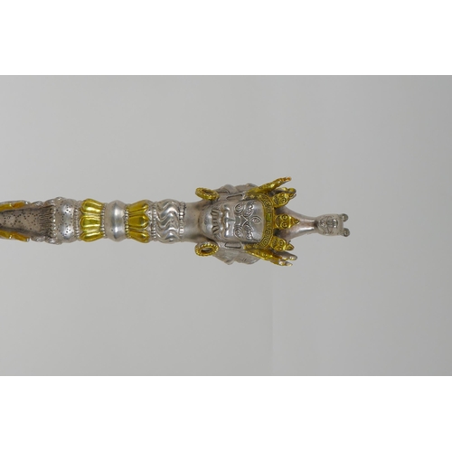 195 - A Tibetan white metal phurba and stand, with gilt highlights, the hilt decorated with wrathful masks