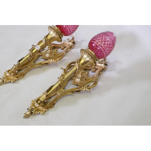 199 - A pair of ormolu wall sconces of trumpet form with leaf swags and cranberry glass shades, 63cm high