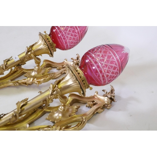 199 - A pair of ormolu wall sconces of trumpet form with leaf swags and cranberry glass shades, 63cm high