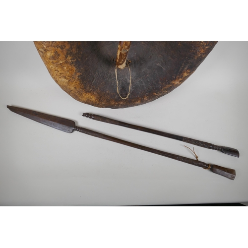 74 - A C19th Ethiopian tribal hide shield and two ceremonial hardwood spears, one AF, shield 57cm diamete... 