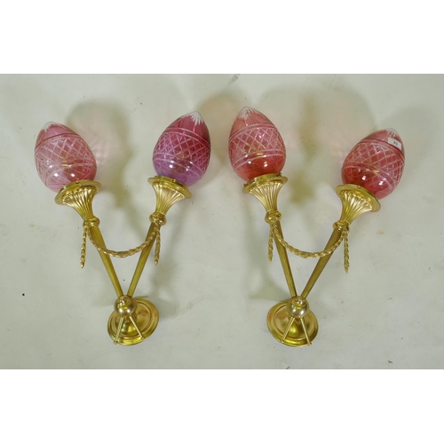 83 - A pair of ormolu two branch wall sconces of trumpet form with cranberry glass shades, 56cm high