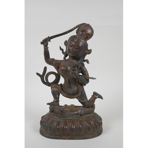 44 - A Tibetan bronze of a sword wielding deity standing over a body, with remnants of gilt patina, 27cm ... 