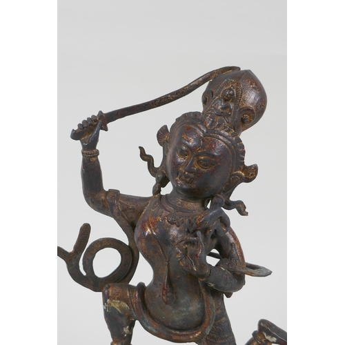 44 - A Tibetan bronze of a sword wielding deity standing over a body, with remnants of gilt patina, 27cm ... 