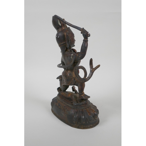 44 - A Tibetan bronze of a sword wielding deity standing over a body, with remnants of gilt patina, 27cm ... 