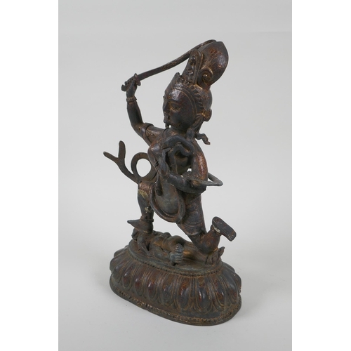 44 - A Tibetan bronze of a sword wielding deity standing over a body, with remnants of gilt patina, 27cm ... 