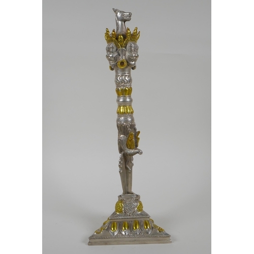 195 - A Tibetan white metal phurba and stand, with gilt highlights, the hilt decorated with wrathful masks