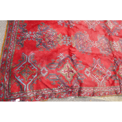 1061 - A full pile wool carpet with geometric designs on a red field, 290 x 385cm