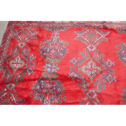 1061 - A full pile wool carpet with geometric designs on a red field, 290 x 385cm