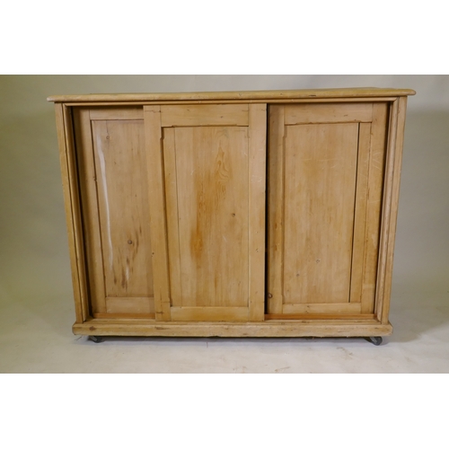 1106 - A C19th pine side cabinet with three sliding doors, on a plinth base with castors, 126 x 48 x 98cm