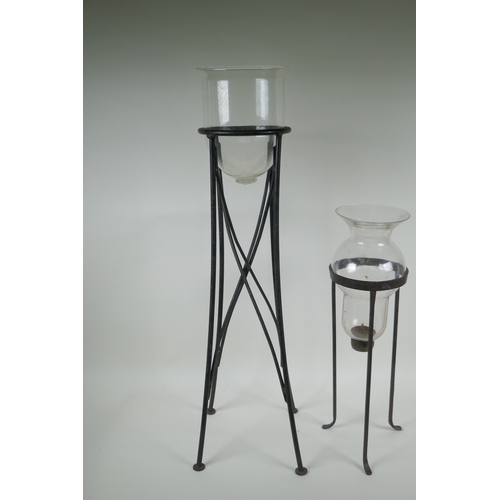 123 - A glass hurricane vase on a wrought iron stand, and another, largest 76cm high