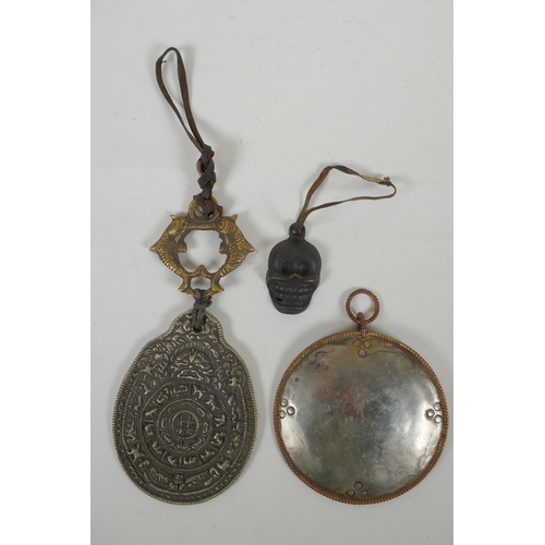 146 - A Tibetan metal calendar, a convex mirror pendant and a cast iron skull pendant, 10cm diameter