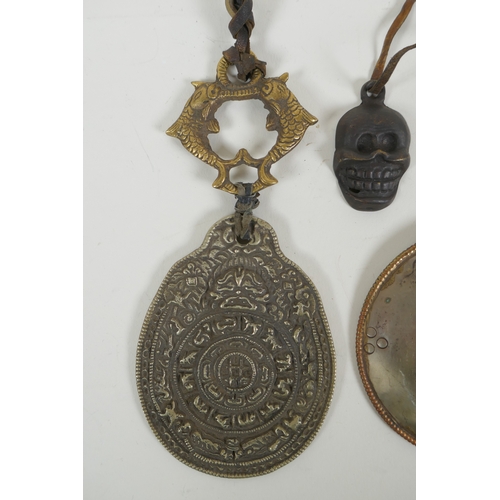 146 - A Tibetan metal calendar, a convex mirror pendant and a cast iron skull pendant, 10cm diameter