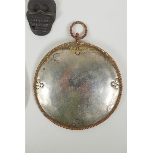 146 - A Tibetan metal calendar, a convex mirror pendant and a cast iron skull pendant, 10cm diameter