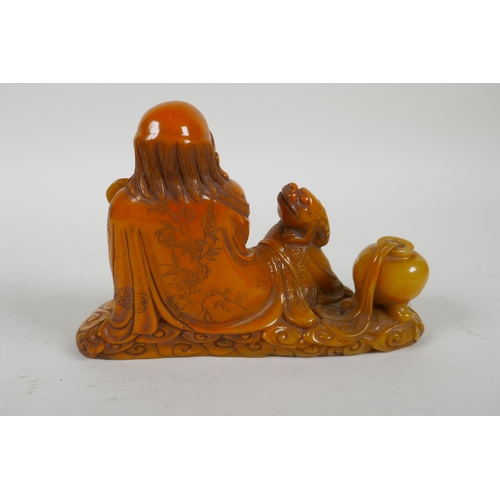 215 - A Chinese imitation amber soapstone carving of Lohan, the base carved for seal, 16cm long