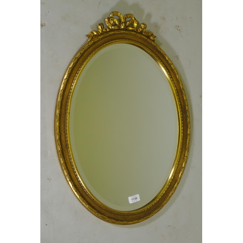 1136 - A gilt oval wall mirror with ribbon decoration and bevelled glass, 71 x 50cm