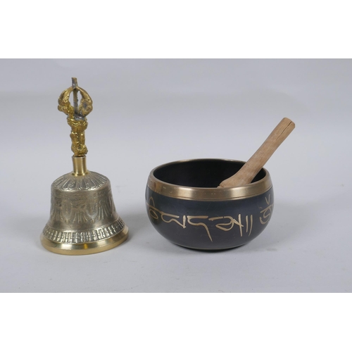 183 - A Tibetan bronze singing bowl with script decoration and wood beater, and a brass ceremonial bell wi... 