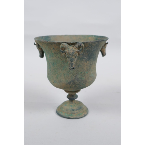 33 - An antique metal goblet with rams head mounts, and green patina, 12cm high