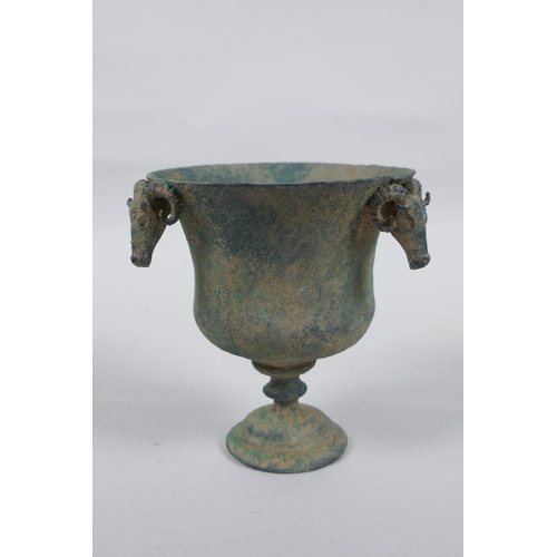 33 - An antique metal goblet with rams head mounts, and green patina, 12cm high