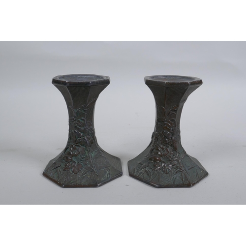 54 - A pair of early C20th Japanese bronze candlesticks of hexagonal waisted form, with raised floral dec... 