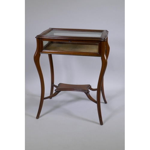 1153 - A mahogany bijouterie cabinet with shaped top, raised on splay supports united by an under tier, 65 ... 