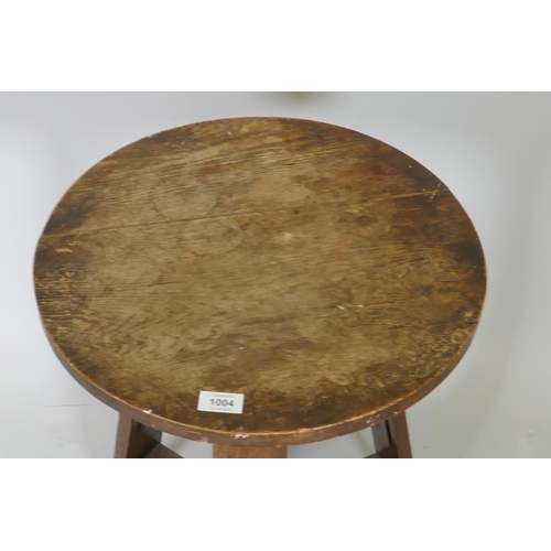 1004 - An Arts & Crafts oak occasional table, the circular top raised on three pierced splay supports u... 