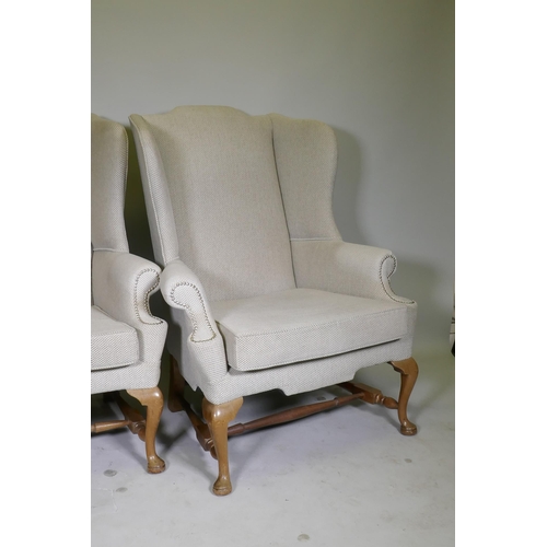 1057 - A good pair of Georgian style high back wing armchairs with wide seats, raised on walnut cabriole su... 