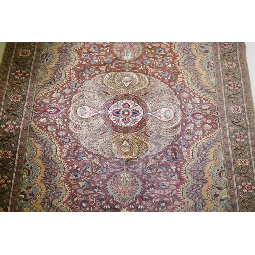 1060 - A Turkish Hereke wool carpet with central design on a faded terracotta field, with blue/grey borders... 