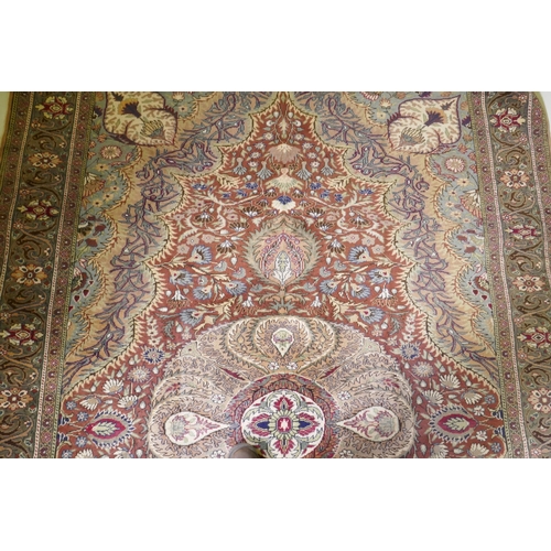 1060 - A Turkish Hereke wool carpet with central design on a faded terracotta field, with blue/grey borders... 