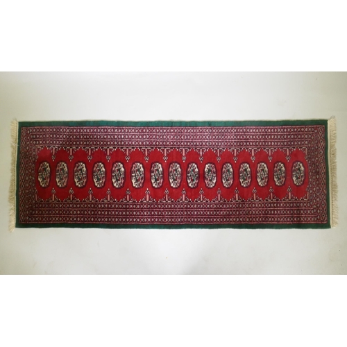 1103 - A Persian red ground wool runner with Bokhara style design and emerald green borders, 64 x 188cm