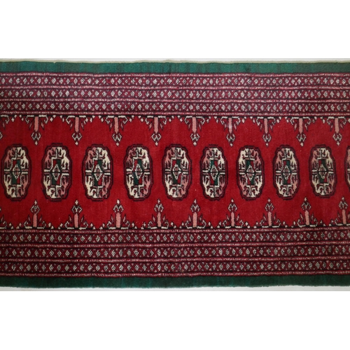 1103 - A Persian red ground wool runner with Bokhara style design and emerald green borders, 64 x 188cm