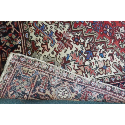 1174 - An antique Persian red and cream ground Heriz full pile carpet with black borders, 210 x 296cm