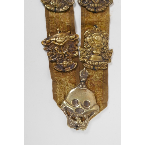 214 - A Tibetan silk sash mounted with brass emblems depicting the Buddhist treasures, 55cm long