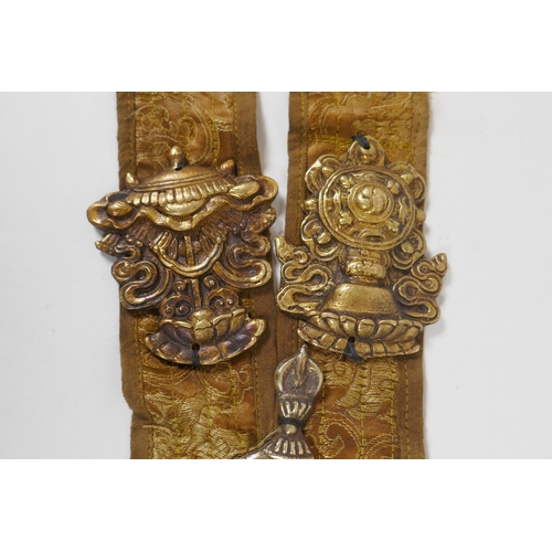 214 - A Tibetan silk sash mounted with brass emblems depicting the Buddhist treasures, 55cm long