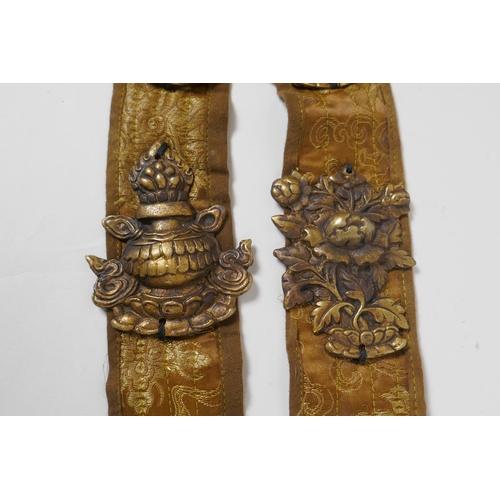 214 - A Tibetan silk sash mounted with brass emblems depicting the Buddhist treasures, 55cm long