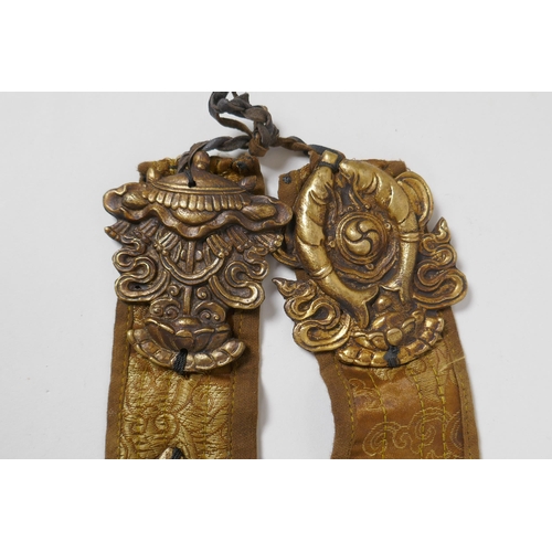 214 - A Tibetan silk sash mounted with brass emblems depicting the Buddhist treasures, 55cm long