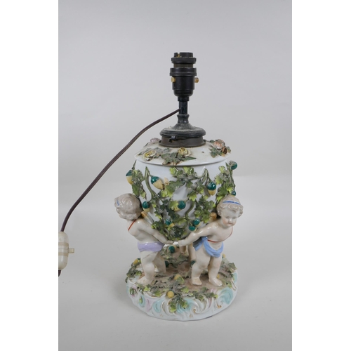 264 - An antique continental porcelain oil lamp converted to electricity, decorated with three winged putt... 