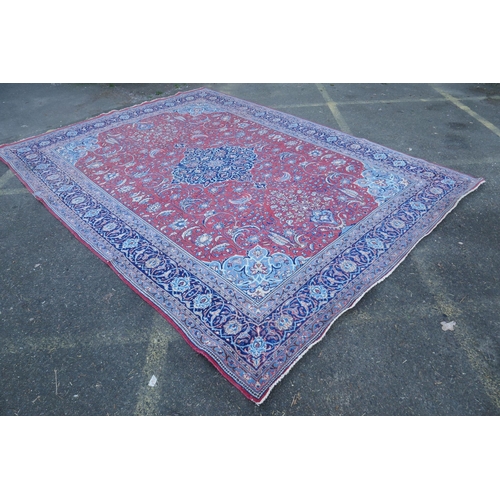 1054 - A large Persian red ground wool carpet with floral medallion design and blue borders, some wear, 74 ... 