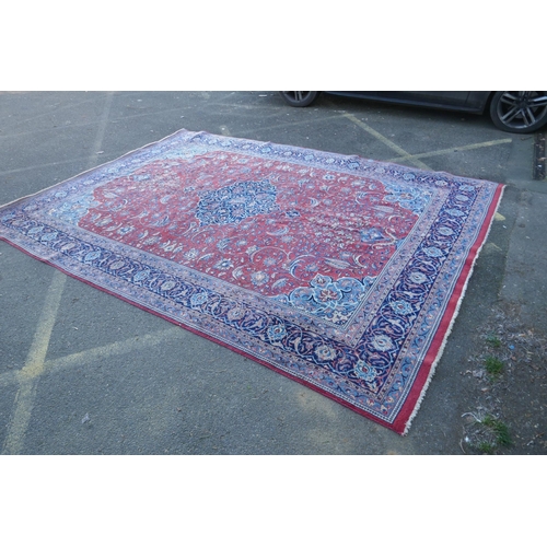 1054 - A large Persian red ground wool carpet with floral medallion design and blue borders, some wear, 74 ... 