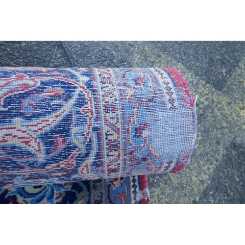 1054 - A large Persian red ground wool carpet with floral medallion design and blue borders, some wear, 74 ... 