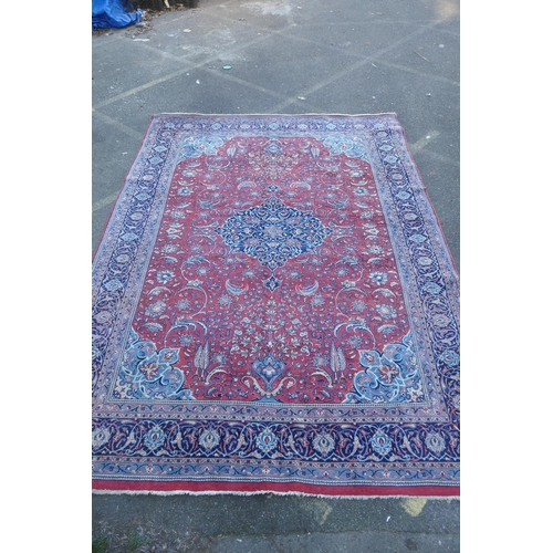 1054 - A large Persian red ground wool carpet with floral medallion design and blue borders, some wear, 74 ... 