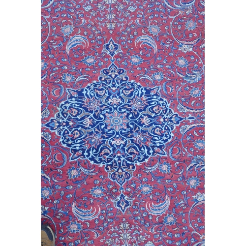 1054 - A large Persian red ground wool carpet with floral medallion design and blue borders, some wear, 74 ... 