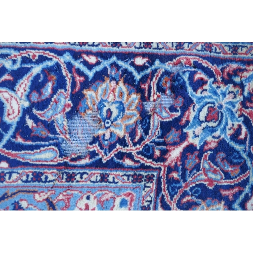 1054 - A large Persian red ground wool carpet with floral medallion design and blue borders, some wear, 74 ... 