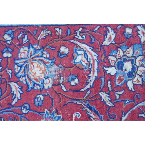 1054 - A large Persian red ground wool carpet with floral medallion design and blue borders, some wear, 74 ... 