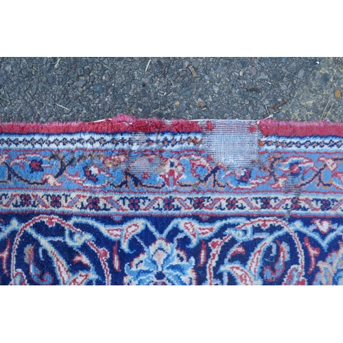 1054 - A large Persian red ground wool carpet with floral medallion design and blue borders, some wear, 74 ... 