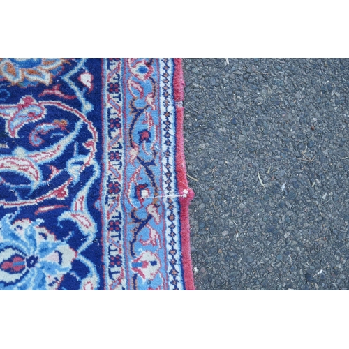 1054 - A large Persian red ground wool carpet with floral medallion design and blue borders, some wear, 74 ... 