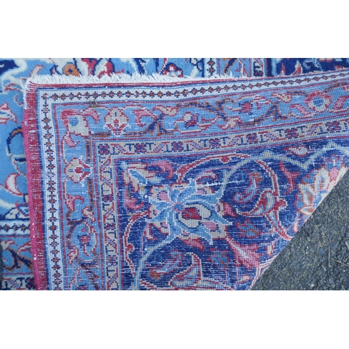 1054 - A large Persian red ground wool carpet with floral medallion design and blue borders, some wear, 74 ... 