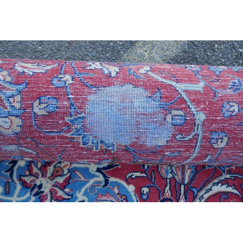 1054 - A large Persian red ground wool carpet with floral medallion design and blue borders, some wear, 74 ... 